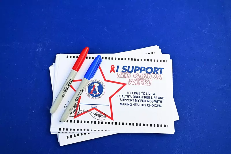A stack of Red Ribbon Week pledge cards reading I support Red Ribbon Week, with a red and a blue marker on top