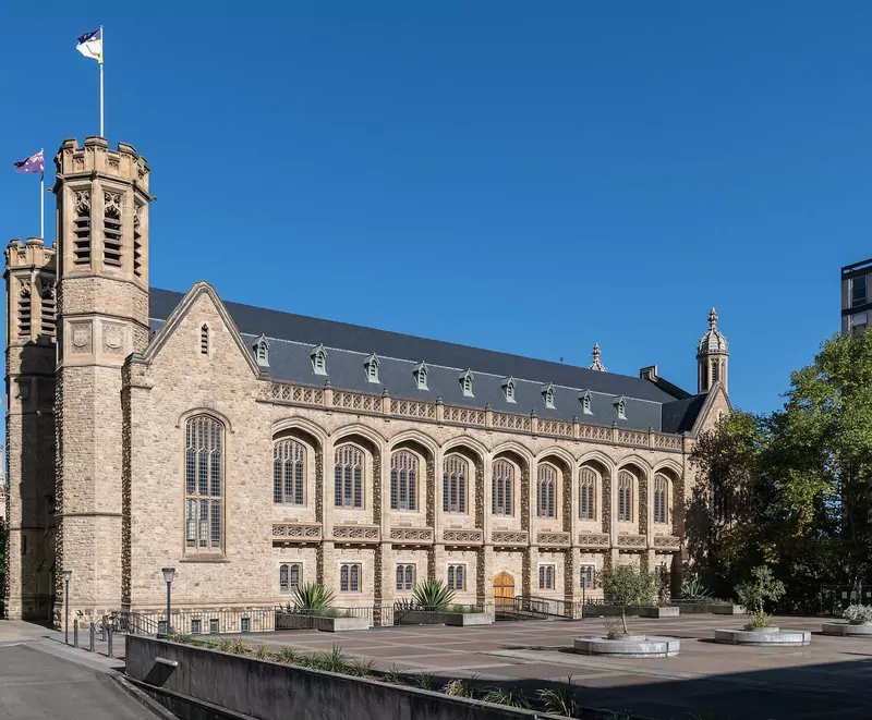The sandstone Bonython Hall at the University of Adelaide, a Gothic-style hall with tall arched windows and a square tower flying flags