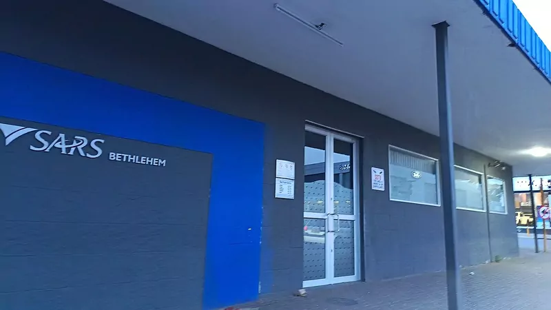 The entrance to the SARS Bethlehem branch: a grey wall with a blue panel and the white SARS logo and the word Bethlehem, a glass door with a small notice board beside it, and a steel pole holding up a covered walkway