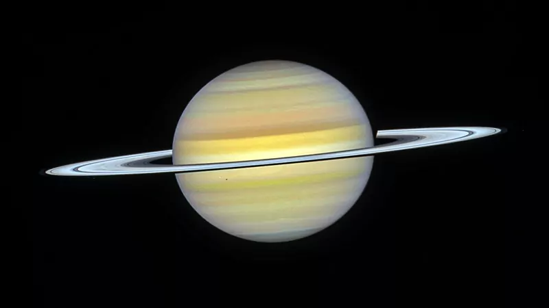 Saturn with pale yellow cloud bands and a thin bright ring seen almost edge-on, photographed by the Hubble Space Telescope