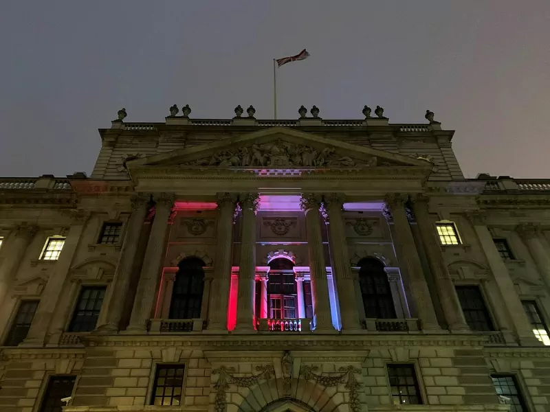 The stone facade of HM Revenue and Customs' building in London at dusk, lit in red, white and blue