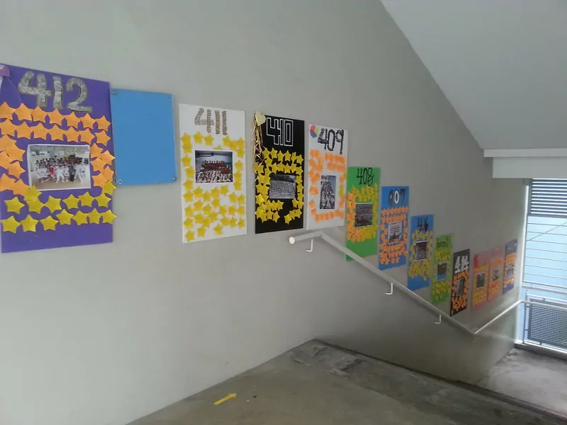 Colourful hand-made posters with class numbers and paper stars taped along a staircase wall
