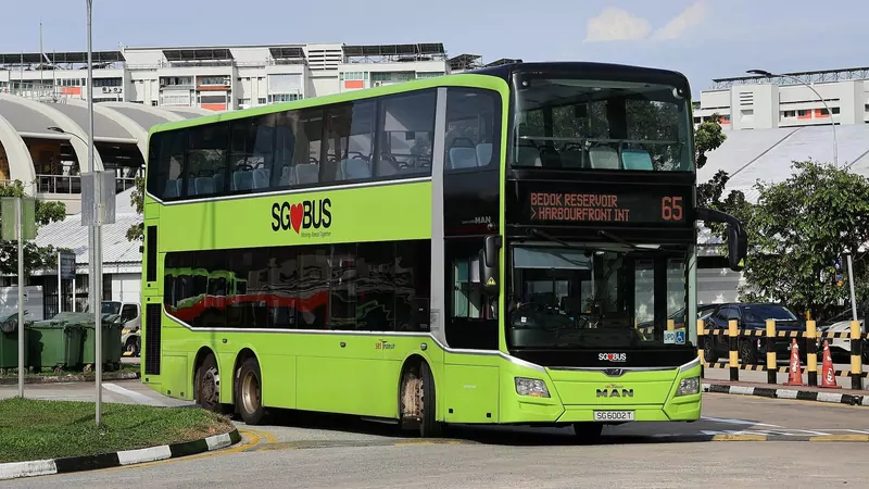 A lime-green SBS Transit double-decker bus with SG Bus branding, on route 65 to Harbourfront, turns past HDB blocks and a curved bus-interchange roof under a blue sky