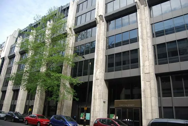 A tall concrete and glass office building in London with trees and parked cars in front