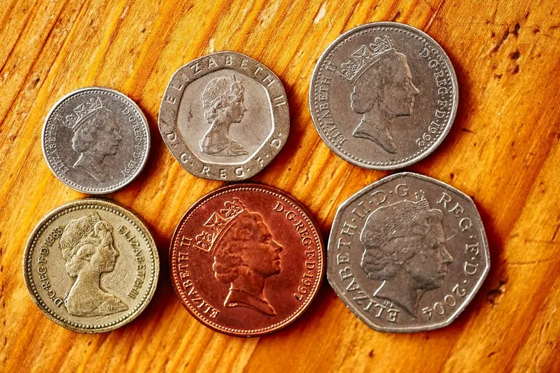Six British coins showing Queen Elizabeth II, including a pound and a fifty pence, on a wooden table