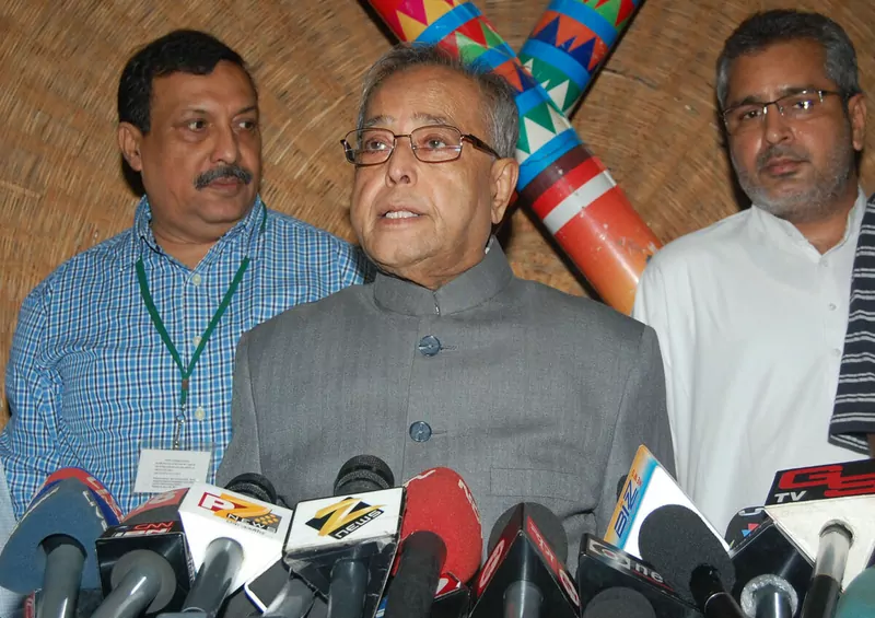 A finance minister speaking into a bank of television microphones, with two officials beside him