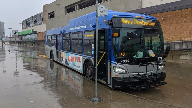 A blue and white Edmonton Transit bus on a wet street with Happy Thanksgiving shown on its front sign