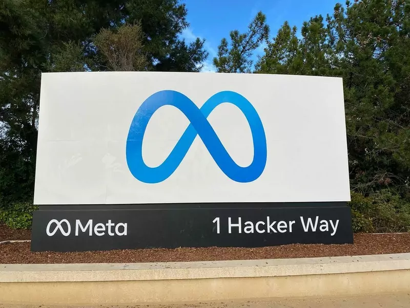A large white sign with the blue infinity-shaped Meta logo and the address 1 Hacker Way, in front of trees