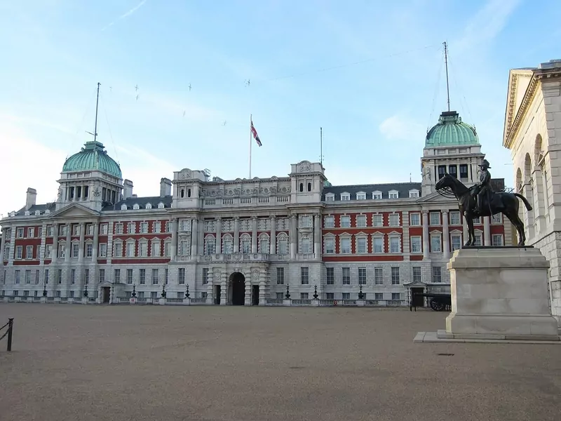 The red-brick and stone Old Admiralty Building with two green domes, seen across the open gravel of Horse Guards Parade, with an equestrian statue on the right