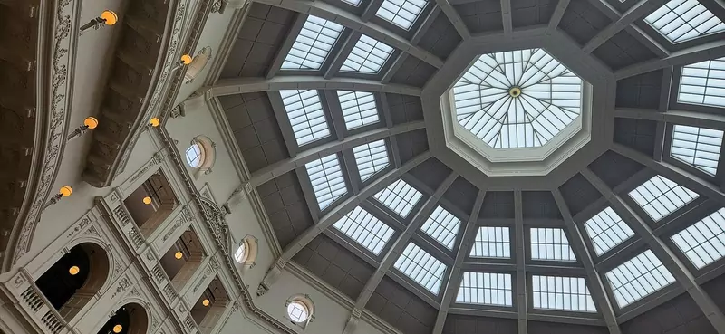 Looking up into an octagonal glass dome with rows of skylight panels and ornate white balconies around its base