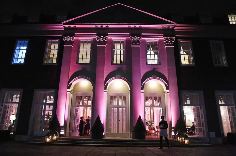 The front of a Georgian mansion lit up in pink at night