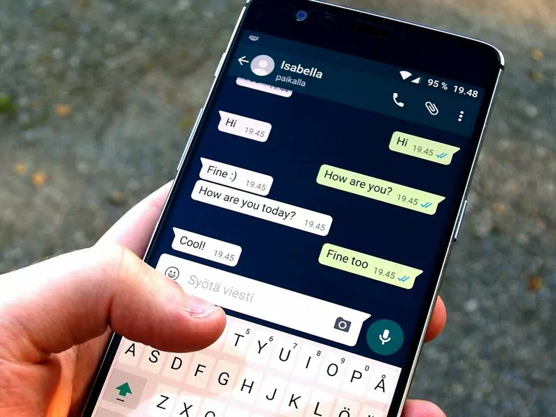 A hand holding a phone showing a short WhatsApp chat and the on-screen keyboard