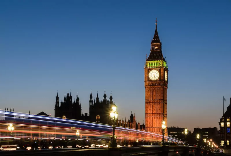 Big Ben's clock tower lit up at sunset, with light trails from traffic on Westminster Bridge