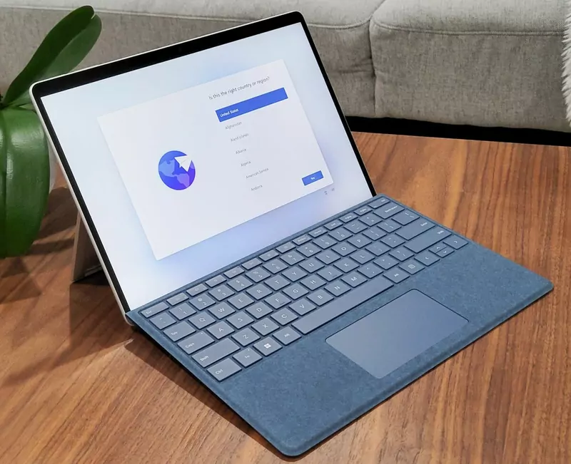 A Surface Pro 9 with a sapphire keyboard on a wooden table, showing a Windows 11 setup screen