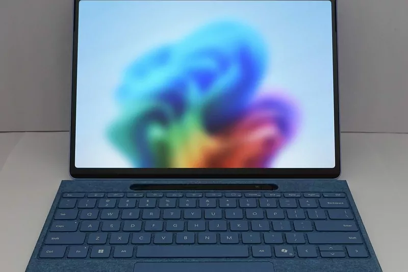 A Microsoft Surface Pro with a blue keyboard cover showing the colourful Windows 11 wallpaper