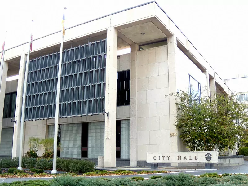 Winnipeg City Hall, a pale stone office building with vertical metal screens, flagpoles and a low City Hall sign in front