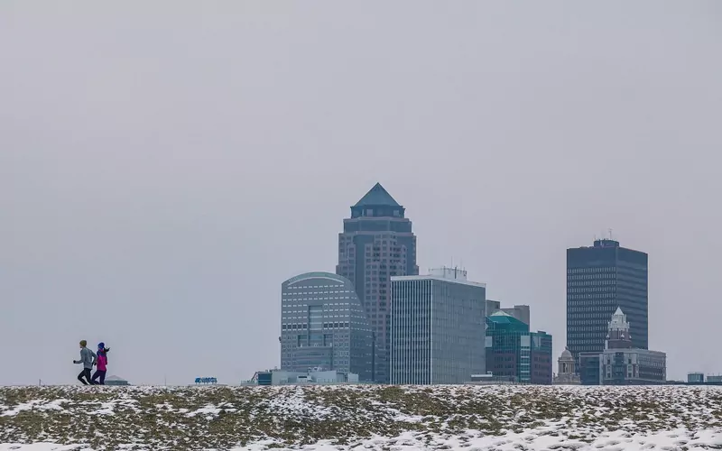 Two joggers running along a snowy trail in the early morning, with the Des Moines skyline in the distance