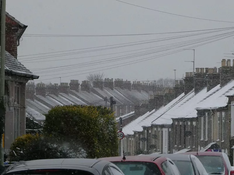 Snow on the roofs of a long row of terraced houses in Norwich, with cars parked in the street below